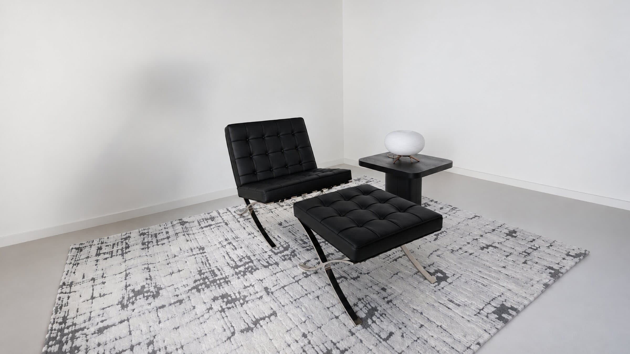 Black leather Barcelona chair and ottoman on a rug against the white cyclorama