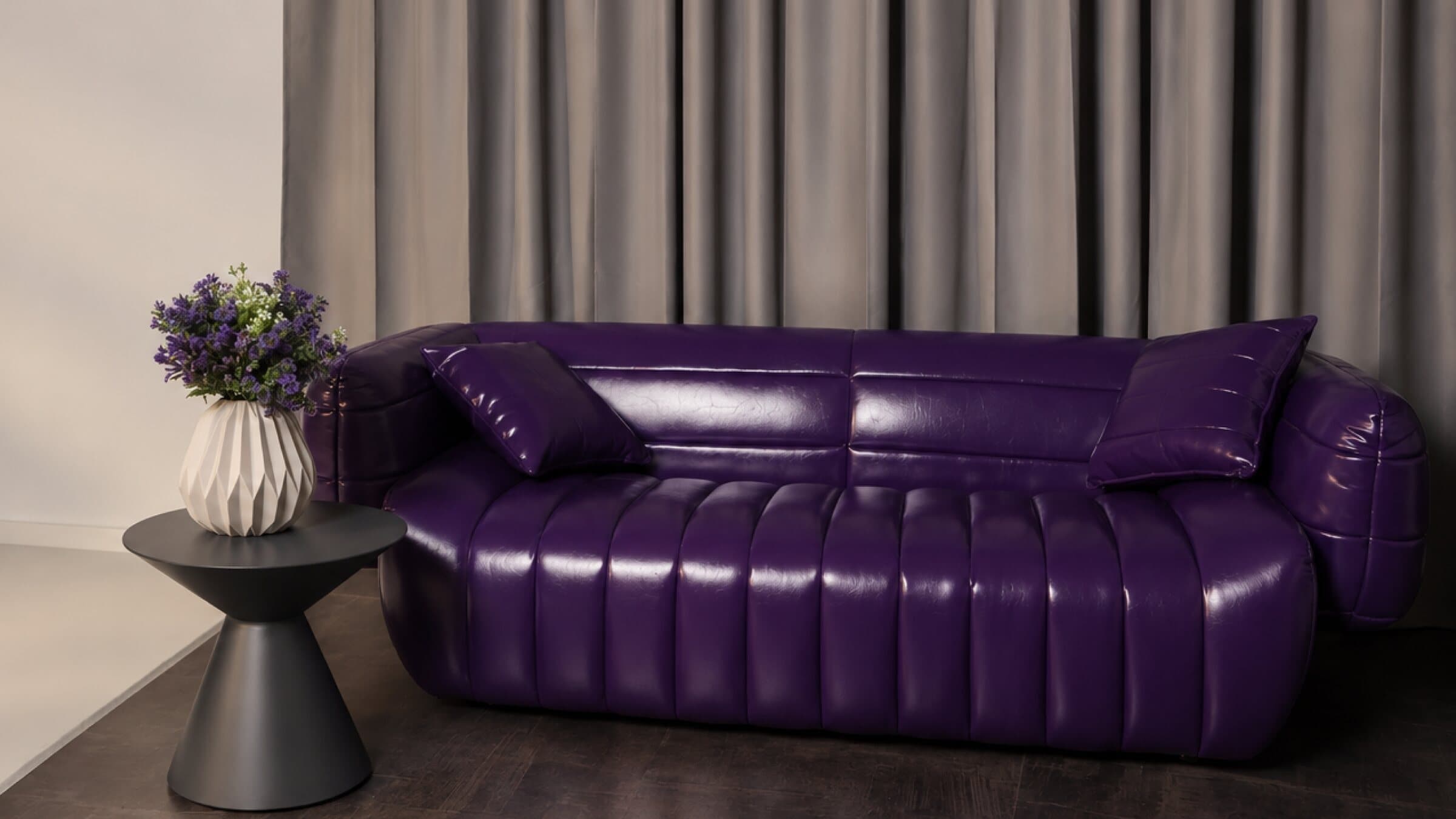 Purple leather sofa with a side table and flowers in front of grey curtains